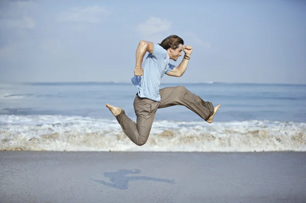 Attractive young man jumping with open legs by the sea shore.