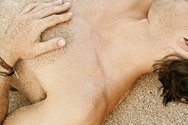 Body part detail of a man sunbathing on a golden sand beach