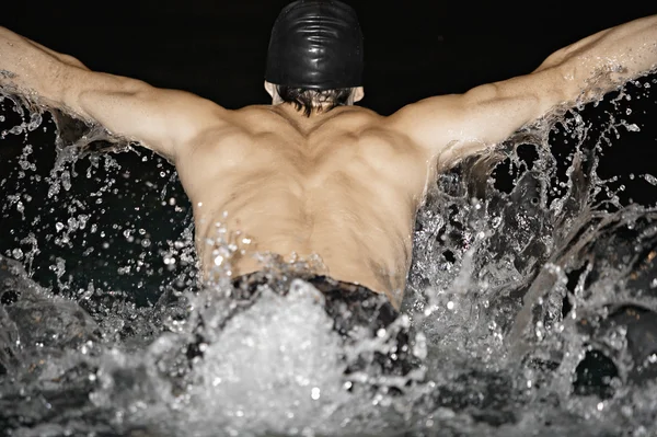 Male swimmer doing butterfly strokes and splashing water in a swimming pool.