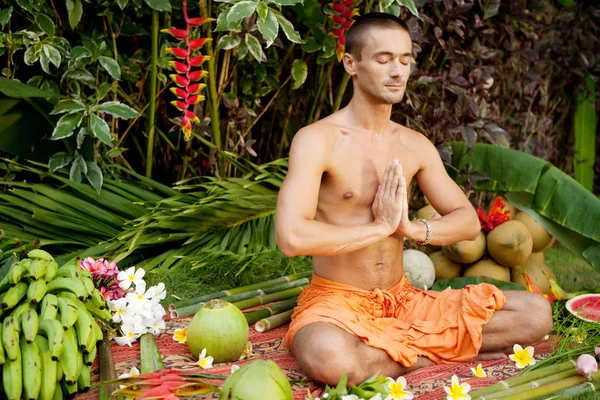 Young man in a yoga position in an exotic garden.