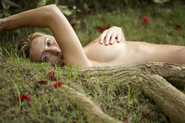 Nude young woman laying down on green grass and red rose petals