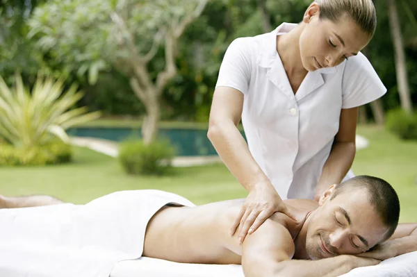 Young man receiving a massage in a tropical garden near a swimming pool.
