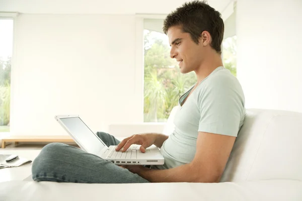 Young man using a laptop computer while sitting down on a sofa at home.