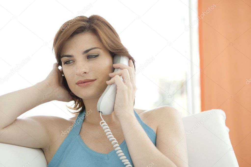 Woman making a phone call at home while sitting on a white sofa