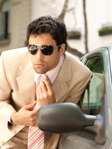 Attractive businessman grooming himself using a car mirror outdoors