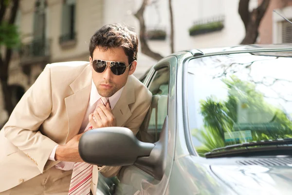 Close up view of an attractive businessman grooming himself using a car mirror outdoors