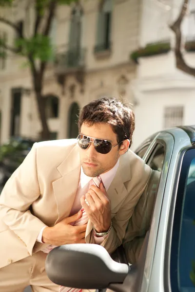 Attractive businessman grooming himself using a car mirror outdoors