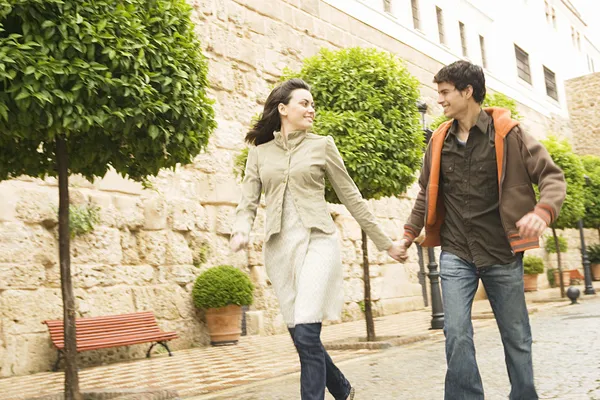Young tourist couple holding hands and running through a town's square.