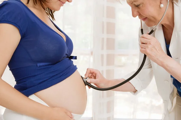 Pregnant woman and doctor uses a stethoscope to listen