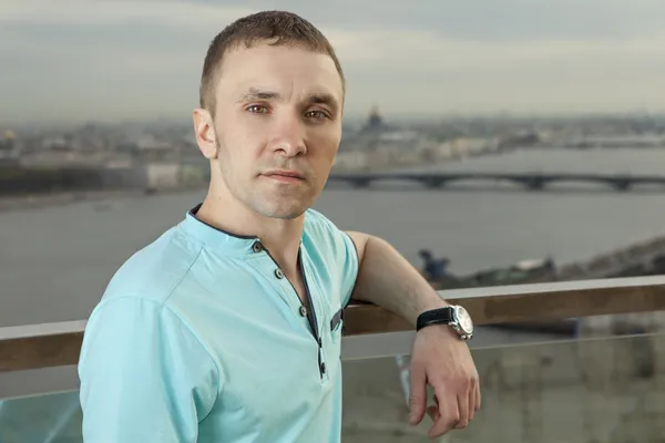A young man in a turquoise shirt, short sleeve, portrait against the background of a European city. One person, a male, short hair. One person, a male, short hair, outdoor, Caucasian, Slav, Russian,