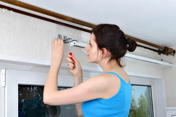 Girl hangs vertical blinds, tighten with a screwdriver, screw br
