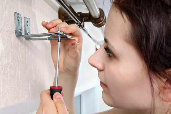 Girl fastens screwdriver bracket vertical blinds to wall.