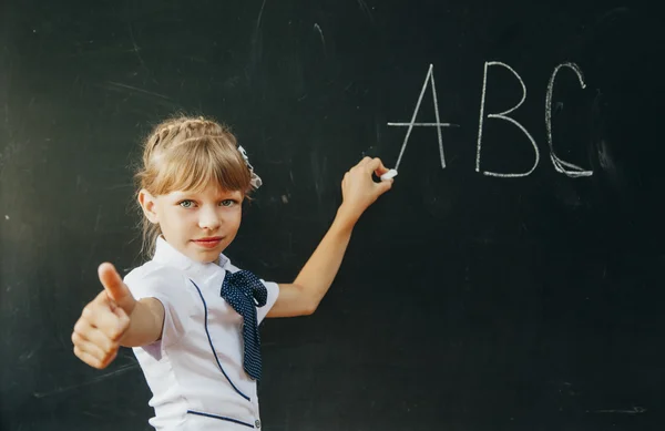 Smiling schoolgirl performs the task at the blackboard.