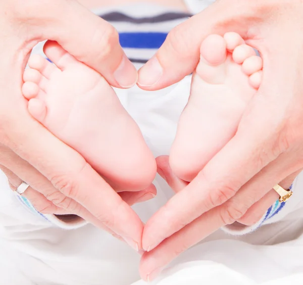 Two hands making a heart around baby feet