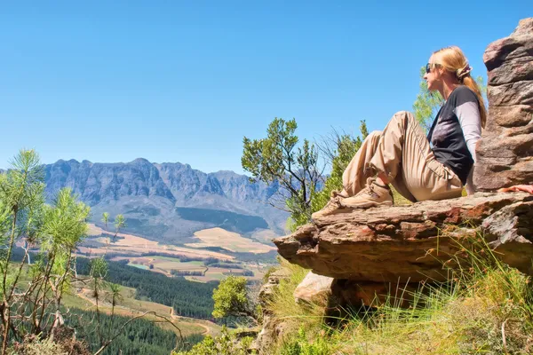 Blonde girl sits on rock and looks at mountains