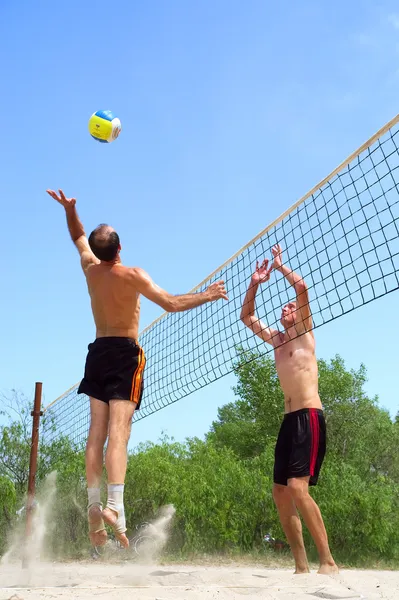 Two men playing beach volleyball - short balding man wins over t