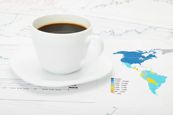 Coffee cup over world map and financial documents