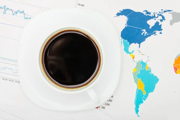 Coffee cup over world map and financial documents - view from top