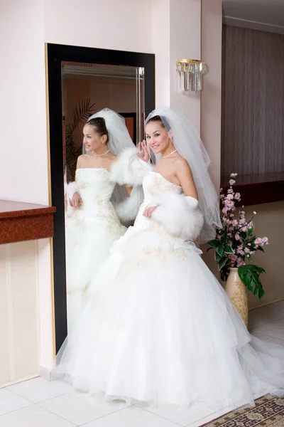 A young bride in a beautiful dress by a big mirror