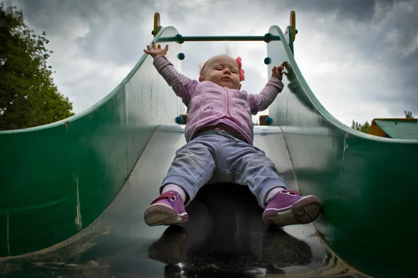 Pretty little girl playing on the playground on the slide