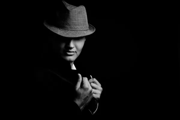 Low key portrait of young gangster with hat in the darkness.