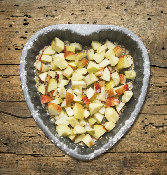 Chopped apples with sugar and sesame seeds in baking dish Heart shaped on old wooden table, top view