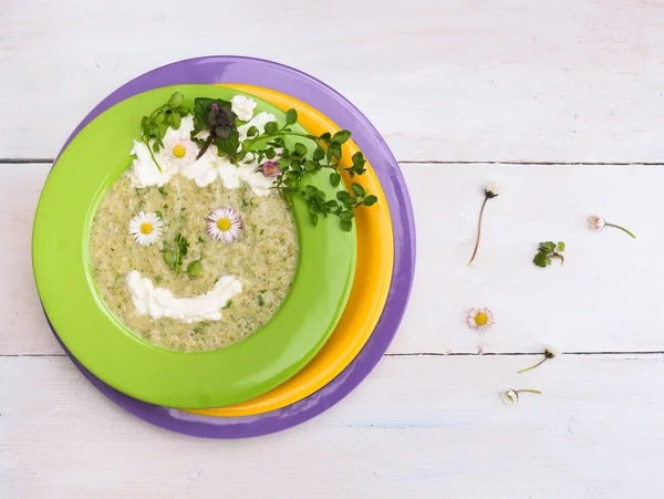 Soup of wild,sprig, herbs, Chickweed,daisy flowers, decorating funny faces  in green, yellow and purple plates