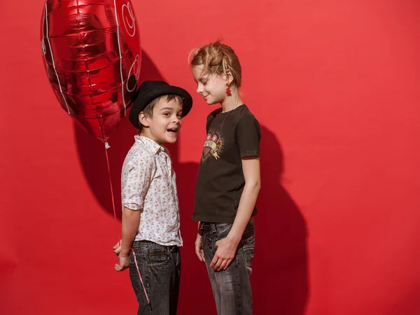Girl and boy with big hearty red balloon on the red background.