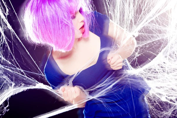Sexy woman with purple wig and intense make-up trapped in a spider web screaming- fashion shoot