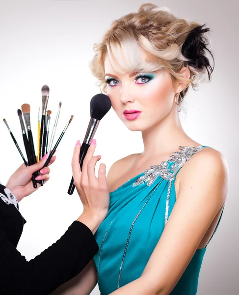 Make-up artist in action on beautiful doll face - blue eyes and blond hair