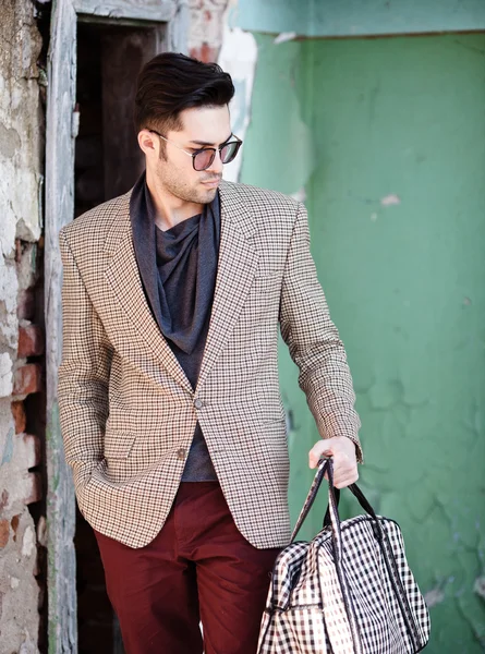 Sexy fashion man model dressed elegant holding a bag posing outdoor