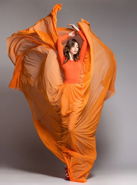 Beautiful woman in long orange dress posing dynamic in the studio
