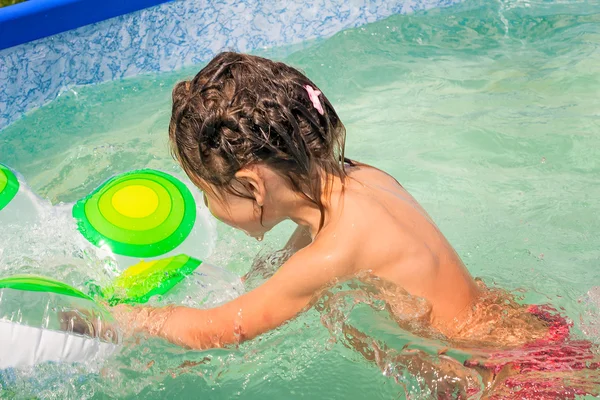 The girl plays in the pool with a rubber ring.