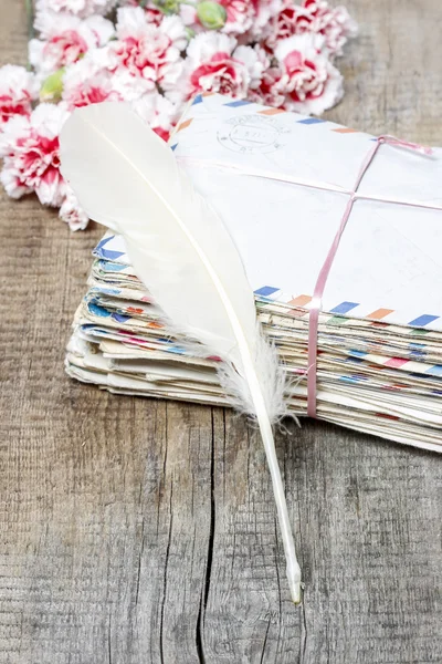 Stack of old letters, feather pen and bouquet of pink carnations