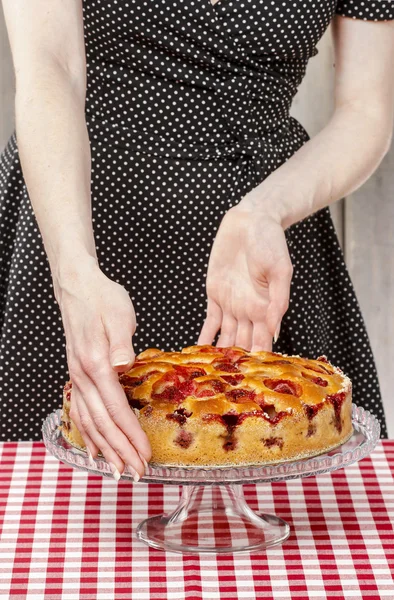 Woman holding strawberry pie on cake stand. Party table