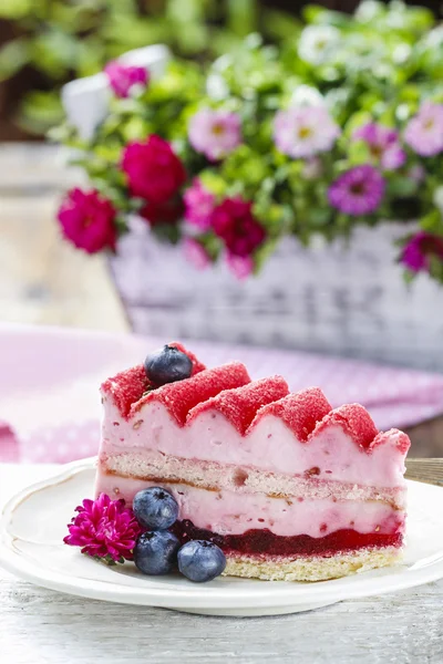 Pink layer cake decorated with fresh fruits on wooden table
