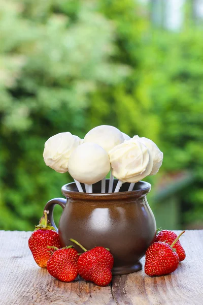 Jug of white cake pops, fresh strawberries around. Summer garden