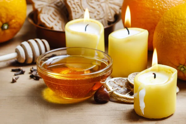 Beautiful candles, bowl of honey and fresh orange fruits on wood