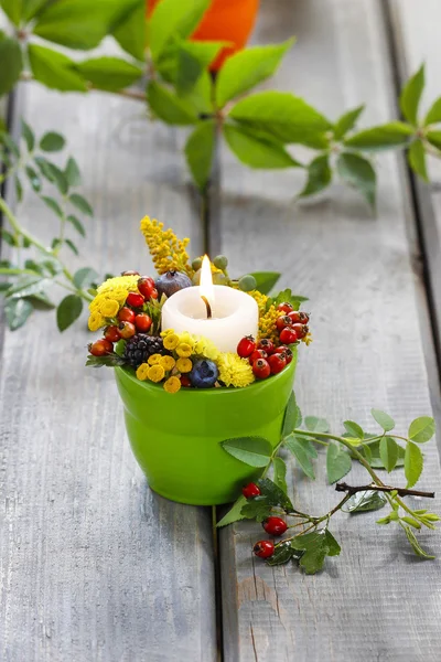 Candle holder decorated with autumn flowers and other plants.