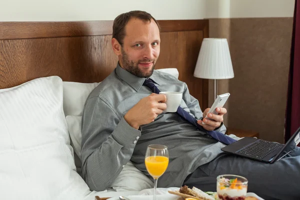 Businessman using phone and laptop during breakfast