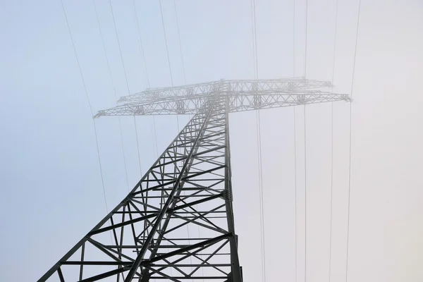 An electricity pylon on a field in the fog