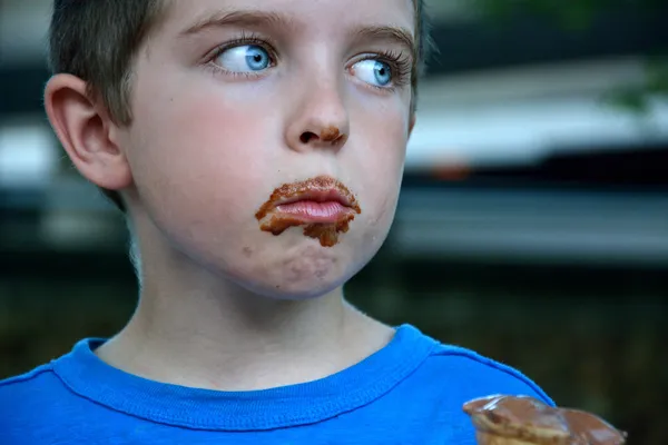 Boy with dirty chocolate face eating ice cream