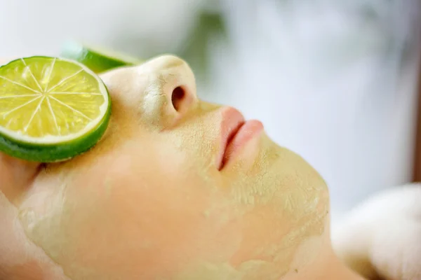 Young woman with green clay mask laying in spa