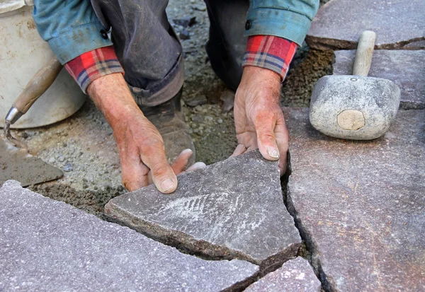 Hands of senior gardener paving natural stone terrace, professional precision work