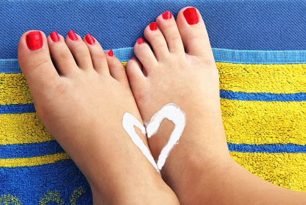 Teenage girls feet on an beach towel with sunlotion heart