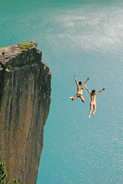 Two cliff jumping girls, against turquoise ocean