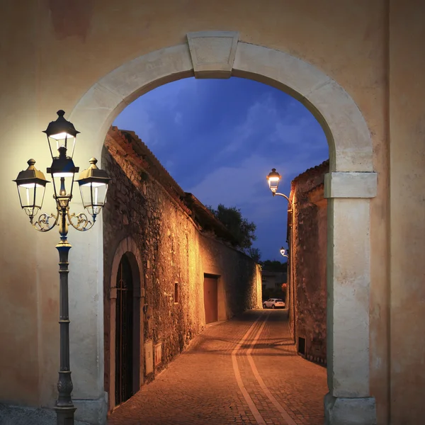Moody illuminated alleyway with arched gate and burning lantern