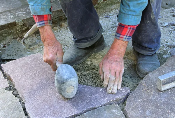 Senior landscape gardener fitting a flagstone tile with a rubber