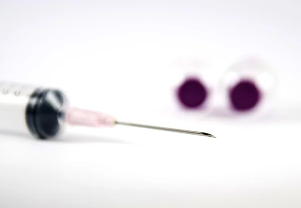 Closed up needle of disposable syringe and purple cap ampule