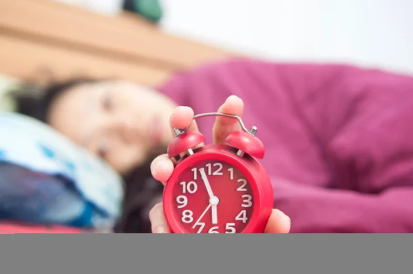 Woman snoozing a red alarm clock